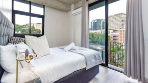 Un dormitorio moderno con una cama grande, una lámpara de noche y vistas de la ciudad desde un balcón.