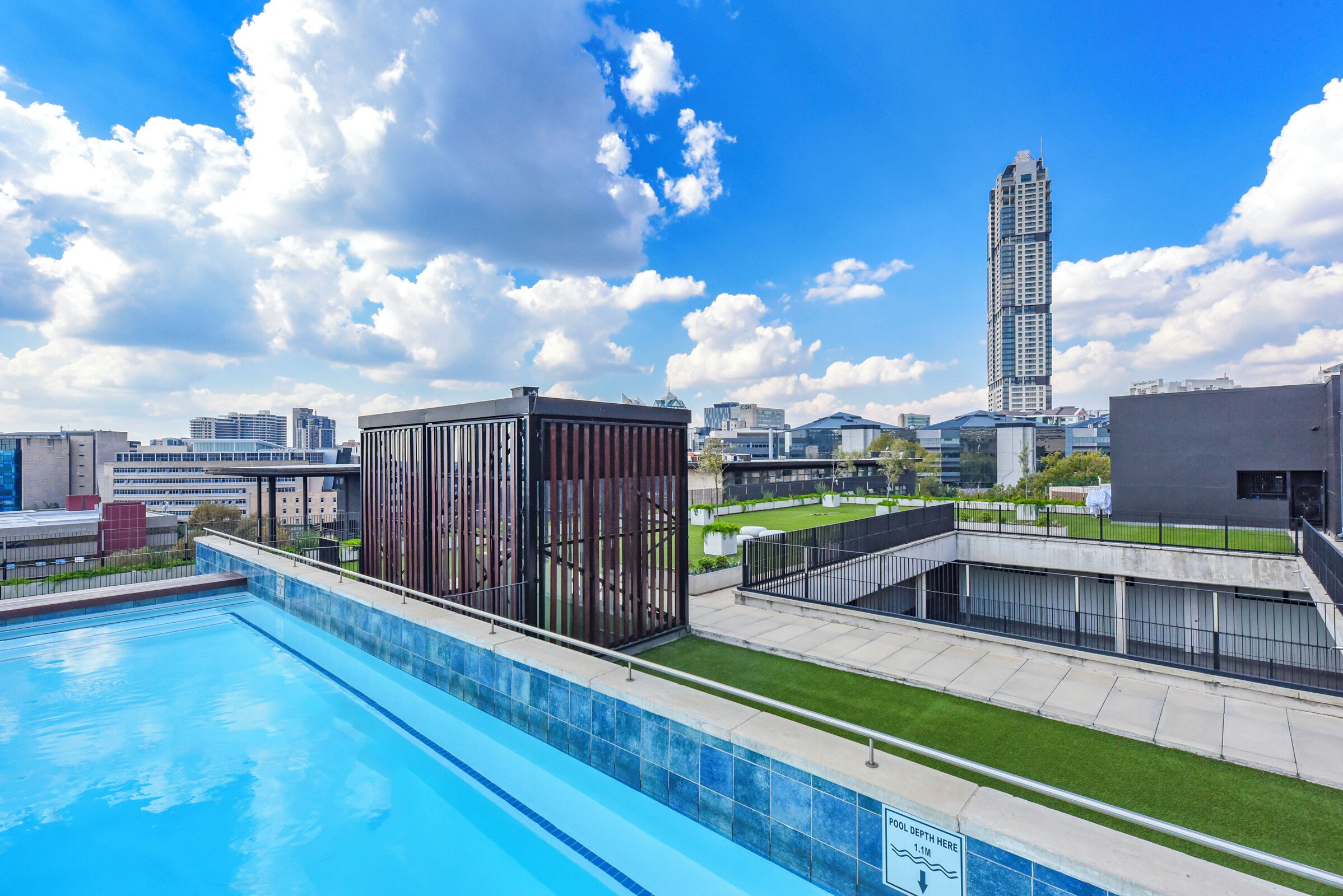 Une piscine avec une structure de bâtiment moderne en arrière-plan, un ciel dégagé et un gratte-ciel imposant.