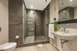 A modern bathroom with a glass-enclosed shower, a white sink, and a toilet. - The Lineal Luxury Apartments - Airscape (Sandton)