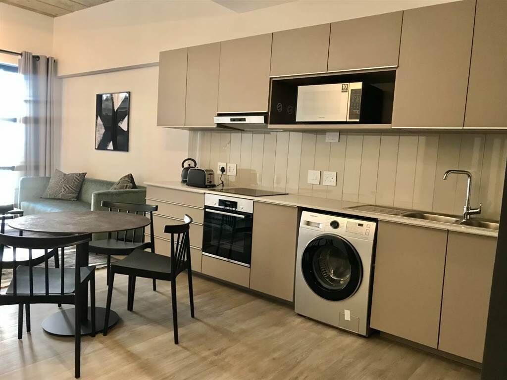 Een compacte keuken met een ingebouwde oven, magnetron en wasmachine. Er is een eettafel met stoelen en een bank in de aangrenzende woonruimte.