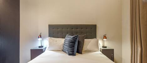 A neatly made bed with a tufted headboard, two bedside lamps, and a dark-colored throw blanket.