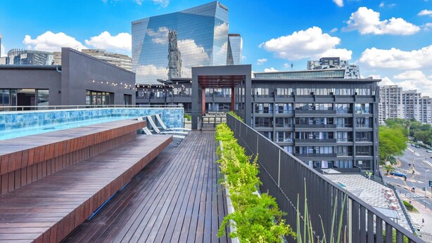 Una terraza en la azotea con piscina, un edificio moderno de fachada de vidrio y vistas a la ciudad.