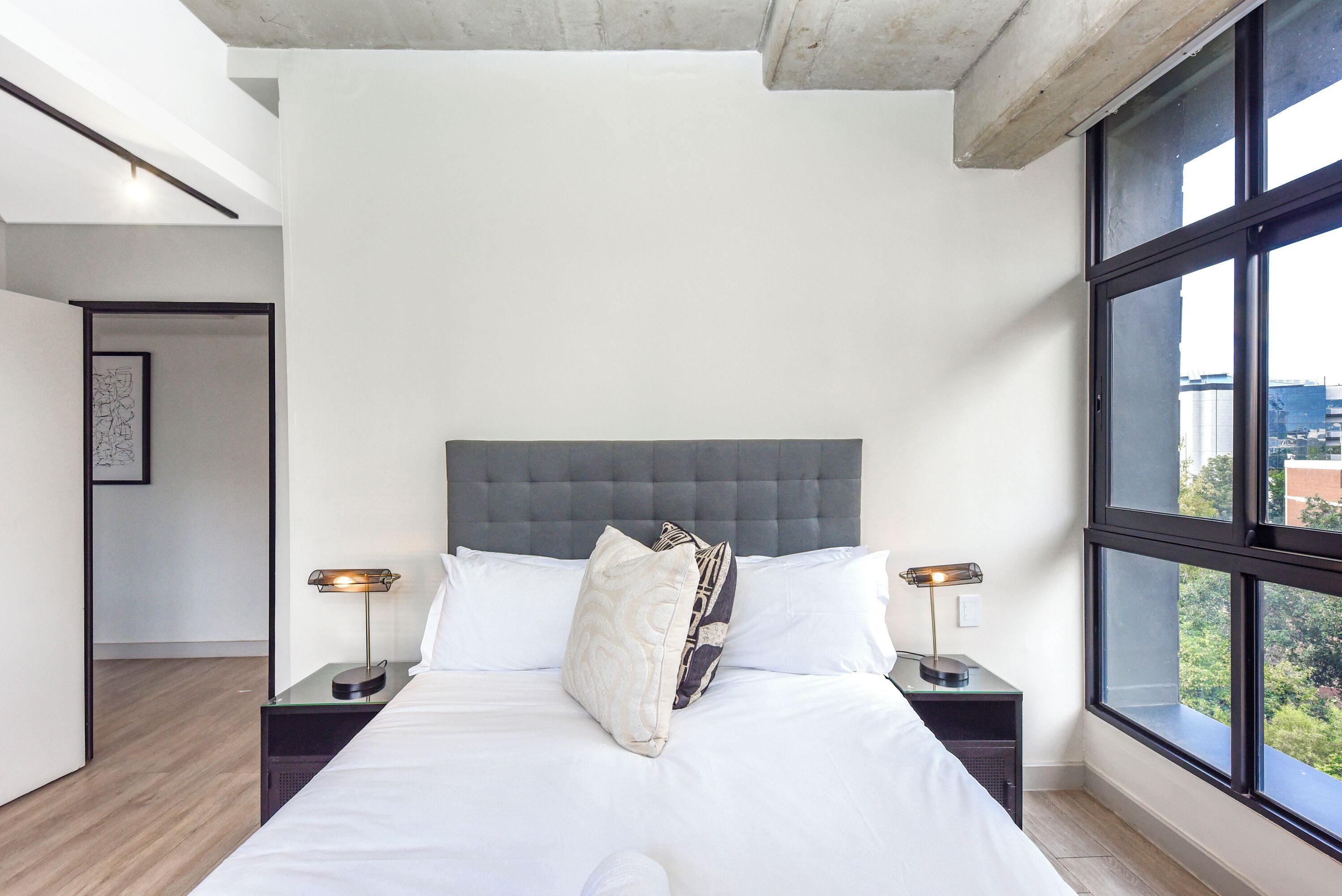 Un dormitorio moderno con una cama grande, dos mesitas de noche y un ventanal amplio.