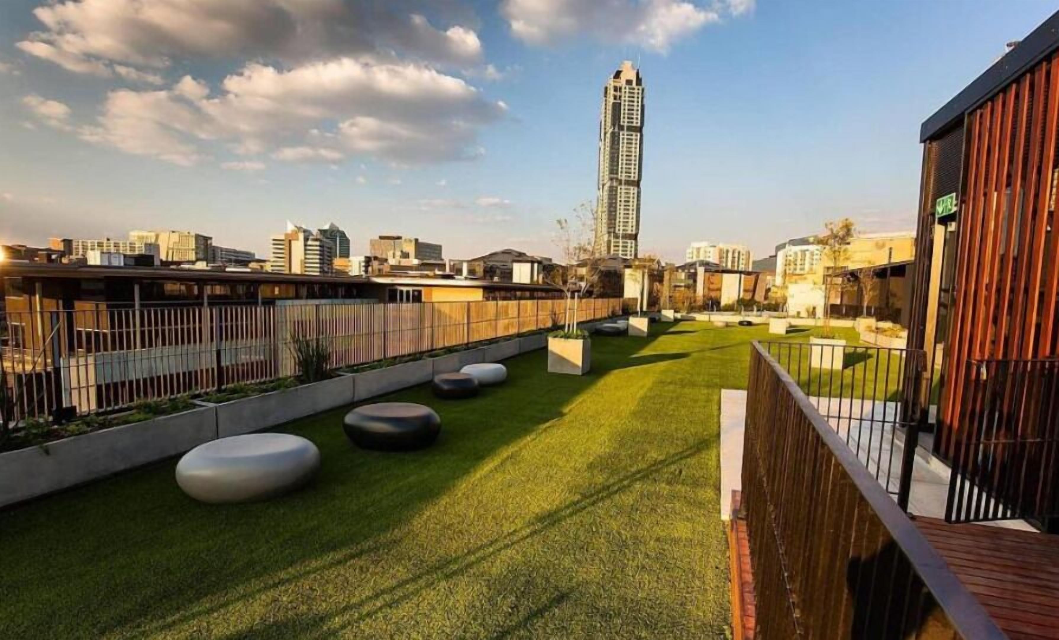Un jardín en la azotea con césped artificial, jardineras y un edificio alto al fondo.