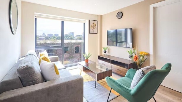 A modern living room with a sofa, a green armchair, a coffee table, and a TV on the wall.