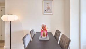 A dining area with a dark wooden table, six chairs, a vase with flowers, and a framed picture on the wall.