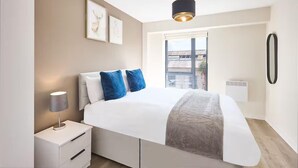 A modern bedroom with a large bed, a bedside table, a lamp, and a window with a view.