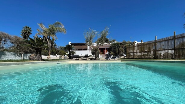 Une piscine d’un bleu éclatant, avec des chaises longues et un bâtiment en arrière-plan.
