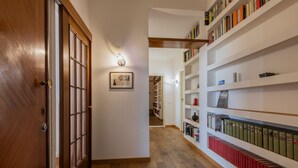 A hallway with wooden flooring, a wooden door, and white walls. There are bookshelves on both sides filled with books. - Casa Andreis by Wonderful Italy (Turin)