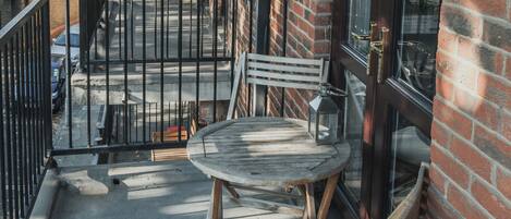 Un balcon avec une table et des chaises en bois, une rambarde en métal et, en arrière-plan, un bâtiment en briques.