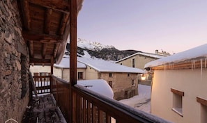 A balcony with stone walls, wooden beams, and a view of snow-covered buildings and mountains in the background. - Charming apartment in Lodenou - Sleeps 7 - Aussois (Aussois)