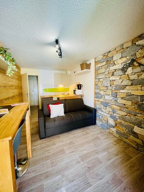 A compact living space with a kitchenette, a sofa, a wooden dining table, and a stone accent wall.