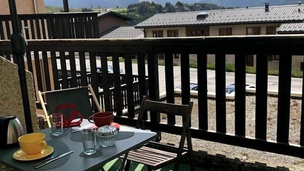 Un balcon avec une table, des chaises et un parasol vert.