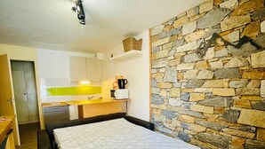 Une petite pièce comprenant un lit, un coin cuisine et un mur en pierre.