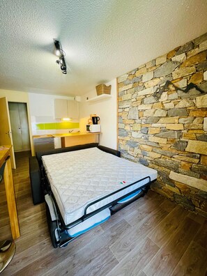 A compact room with a bed, kitchenette, and a stone wall. - Studio/ terrace "le Plan sec", 3 pers Aussois (Aussois)