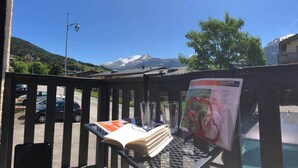 A balcony with a view of mountains, a table with a menu, and parked cars.