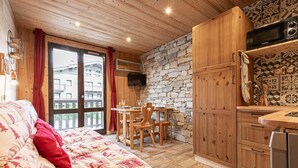 A cozy room with a bed, a dining table with chairs, a stone wall, wooden cabinets, and a TV mounted on the wall.