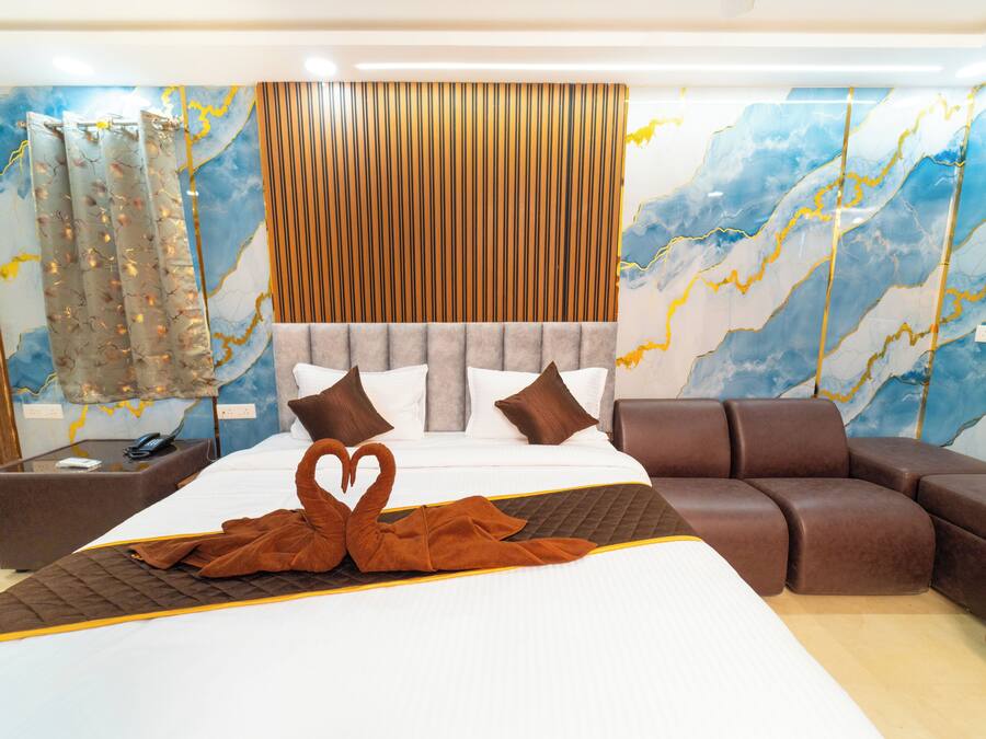 A modern hotel room with a large bed, a brown sofa, and a decorative swan towel arrangement.