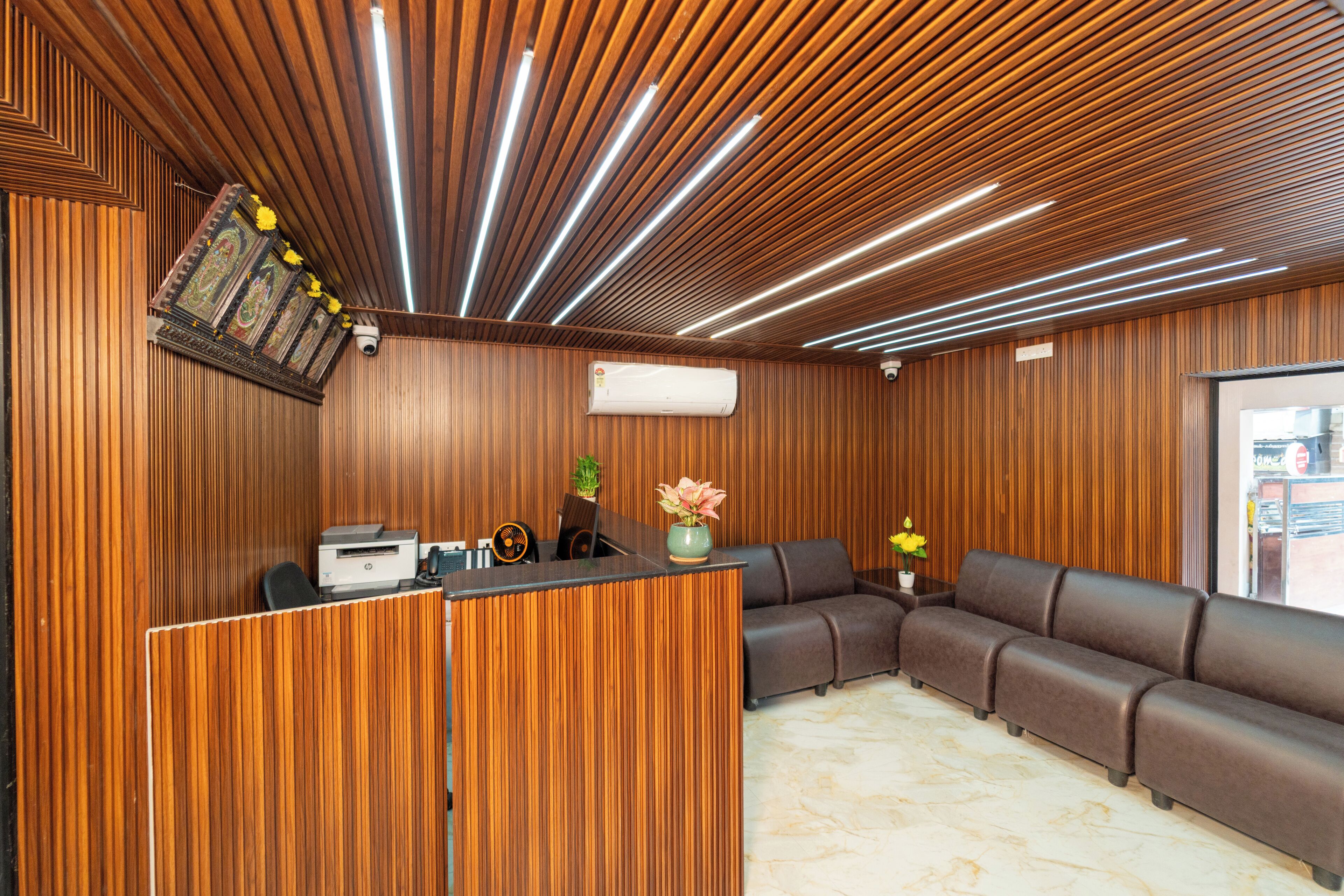A reception area with a wooden panel wall, a reception desk, a brown leather sofa, and a potted plant.