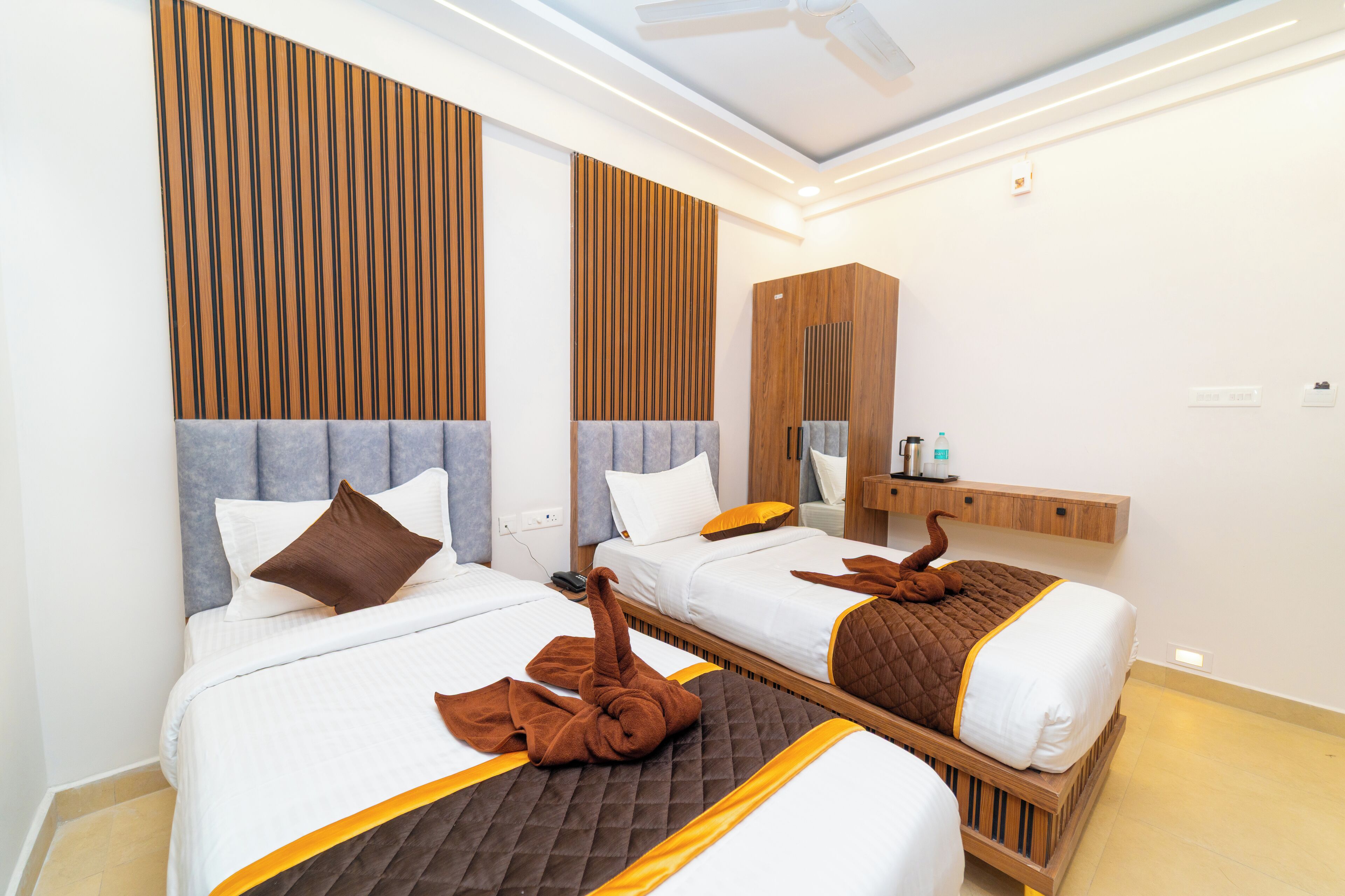 A hotel room with two beds, wooden headboards, a vanity with a mirror, and a ceiling fan.