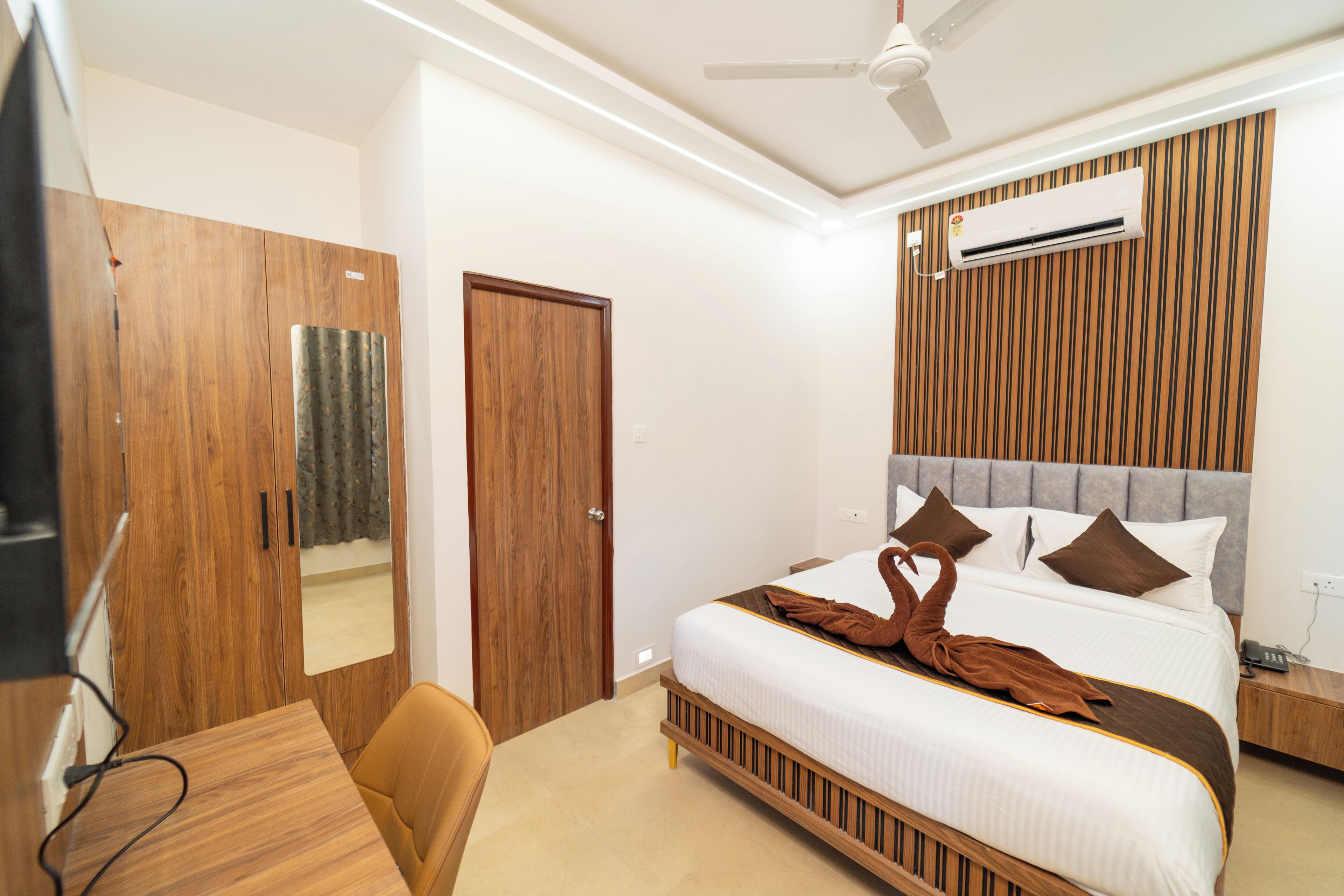 A hotel room with a bed, a desk, a chair, a wardrobe, and an air conditioning unit.