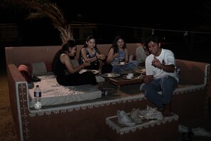 Um grupo de pessoas sentadas em um sofá, com uma mesa à frente, fazendo uma refeição.