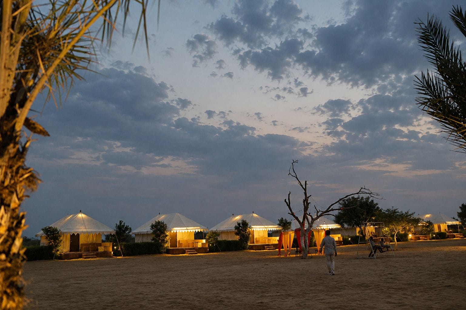 Várias yurts com telhados cônicos, dispostas em fila sobre um terreno arenoso, sob um céu limpo.