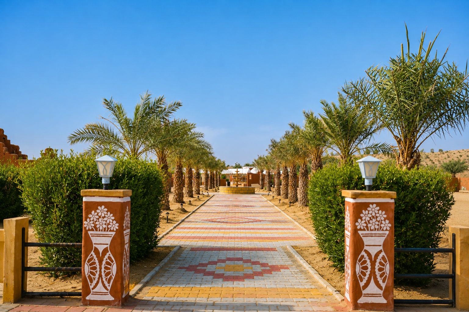 A pathway leading to a building with a patterned tile floor, flanked by palm trees and decorative pillars with floral designs.