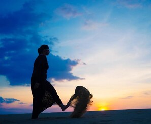 A silhouette of a person walking on a beach at sunset with a logo in the corner. - barna dersert camp jaisalmer (Jaisalmer)