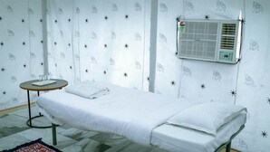Un consultorio médico con una cama, una mesita con una bandeja y un aire acondicionado instalado en la pared.