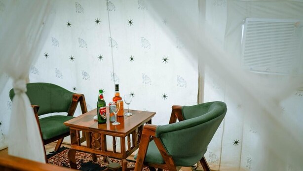 Una habitación acogedora con una mesa de madera, dos sillas verdes y una cortina estampada.