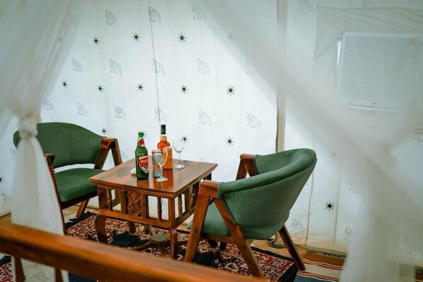 A cozy room with a wooden table, two green chairs, and a patterned curtain. - barna dersert camp jaisalmer (Jaisalmer)