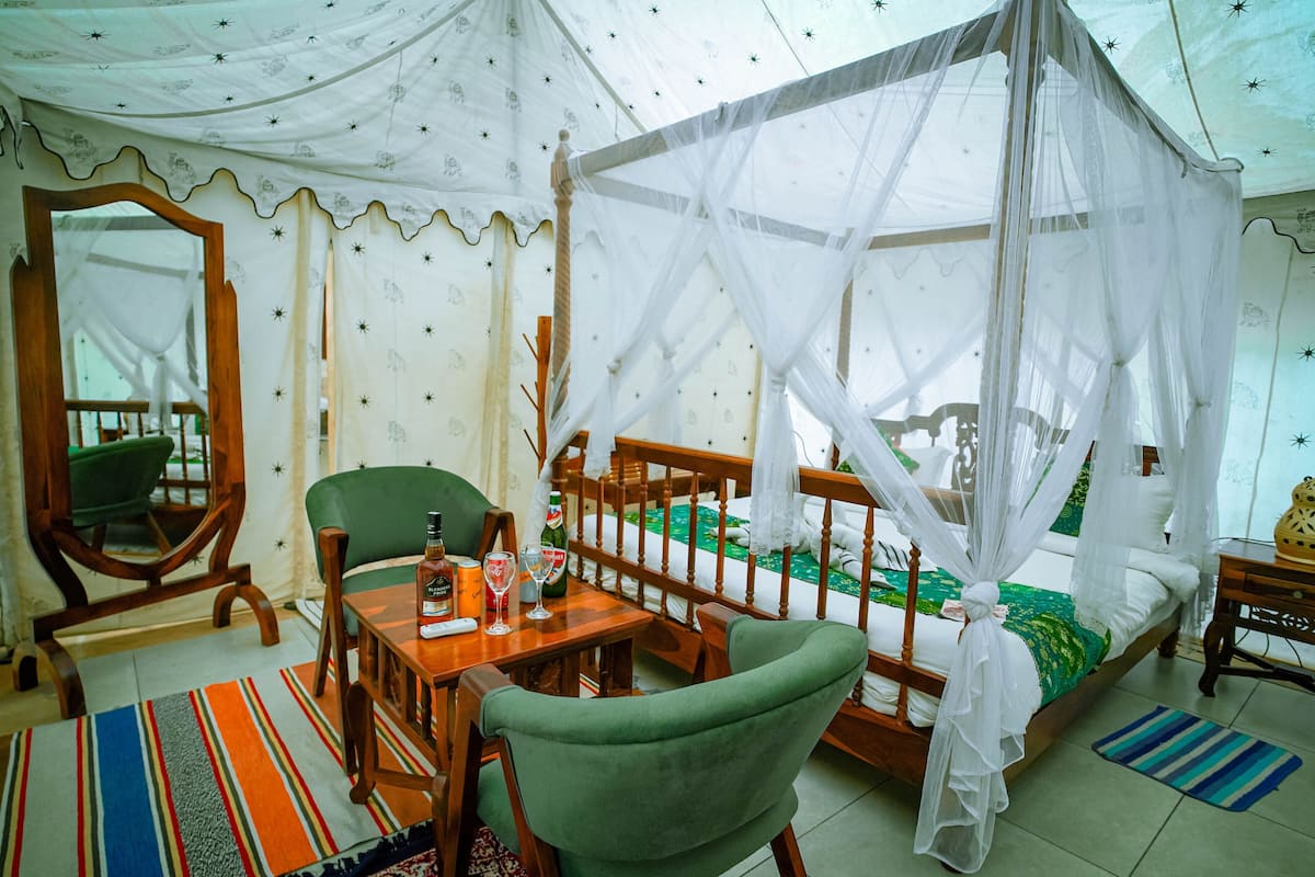 A room with a bed under a canopy, a wooden chair, a table with bottles, and a striped rug.