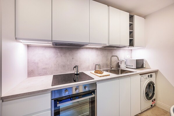 A compact kitchen with white cabinets, a built-in oven, a microwave, and a washing machine.