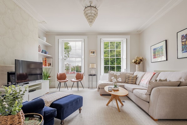 A living room with a television, two chairs, a sofa, a coffee table, and a chandelier. - Stylish 5BD Townhouse in Leamington Spa (Royal Leamington Spa)