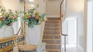 A hallway with a staircase, a mirror, and two white textured vases with flowers.