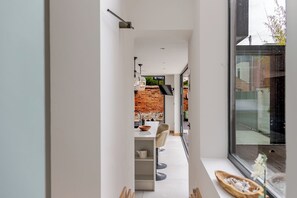 Un corridoio stretto che conduce a una cucina con parete in mattoni, arredamento moderno e un'ampia finestra.