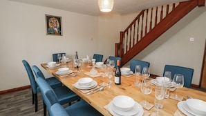 Une salle à manger avec une table en bois dressée pour le repas, des chaises à l’assise rembourrée de couleur bleue et un lustre.