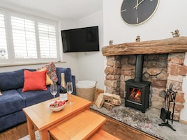 Una sala de estar acogedora con una chimenea de piedra, un sofá azul, una mesa de madera con un cuenco de fresas y copas de vino, y un televisor en la pared.