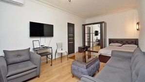 A modern living room with a grey sofa, a grey armchair, a small table, a TV, and a bed with a wooden headboard. - Mashtots  apartment by Luxe Group MA154 (Yerevan)