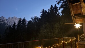 Une terrasse en bois illuminée de guirlandes lumineuses, un luminaire en forme d’étoile et une vue sur les montagnes en arrière-plan.