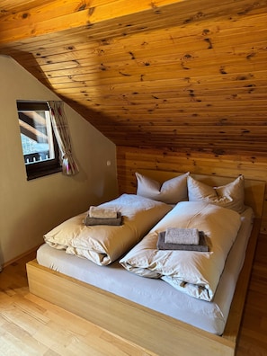 Techo de madera, cama con almohadas y toallas, y una ventana con cortinas.