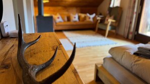 Une table en bois ornée d’une branche de cerf, un canapé et un lit dans une pièce chaleureuse aux murs en bois et au plafond en pente.