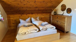 Une chambre avec un plafond en bois, un lit avec des oreillers et des serviettes pliées, une commode en bois et des miroirs fixés au mur.