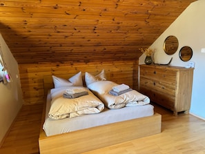 A bedroom with a wooden ceiling, a bed with pillows and folded towels, a wooden dresser, and wall-mounted mirrors.