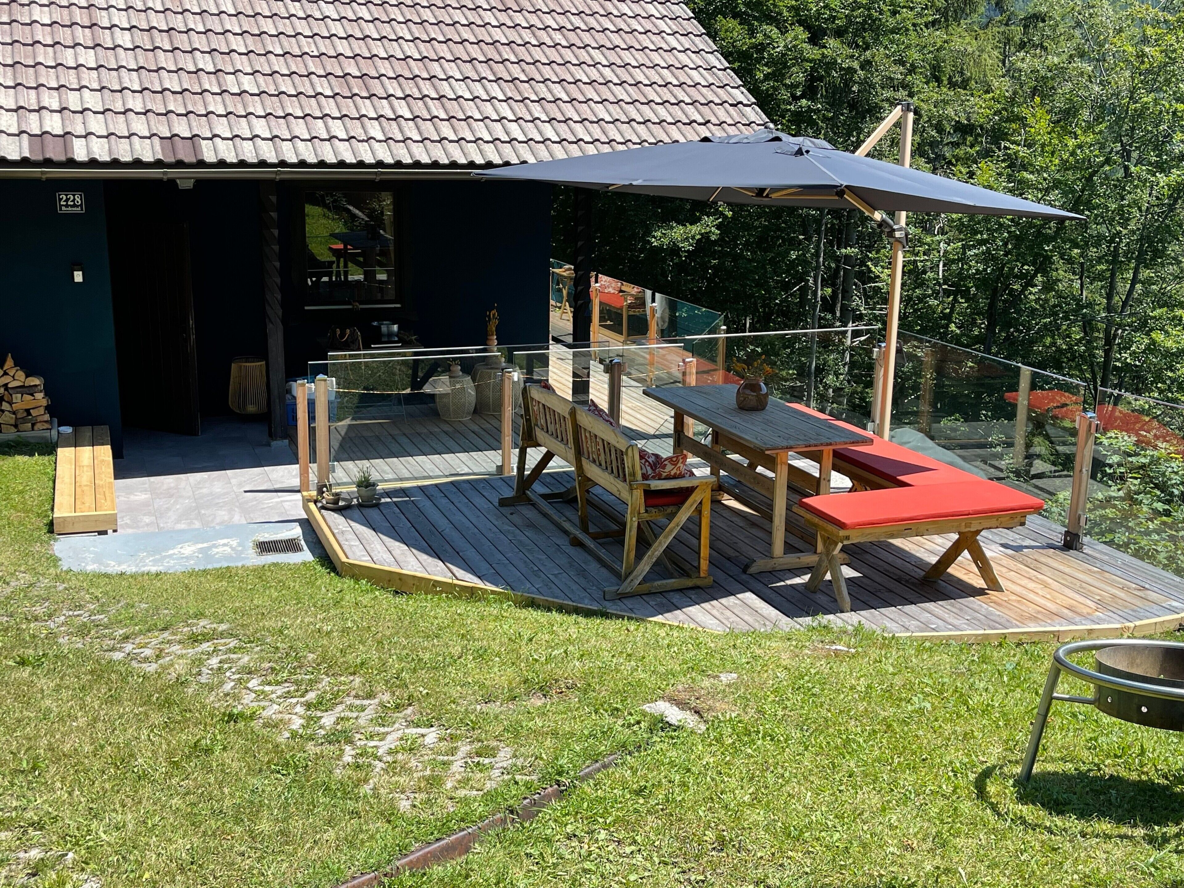 Een houten terras met een tafel en stoelen, een overdekt gedeelte en een ingang van een gebouw.