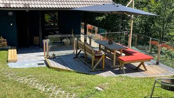 Una terraza de madera con una mesa y sillas, un área cubierta y la entrada a un edificio.