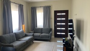 A living room with two grey sofas, a coffee table, a TV on a black stand, and a door with illuminated panels.