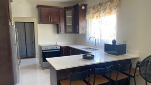 A kitchen with dark wooden cabinets, a white countertop, a stove, a sink, and a small dining area with two chairs.