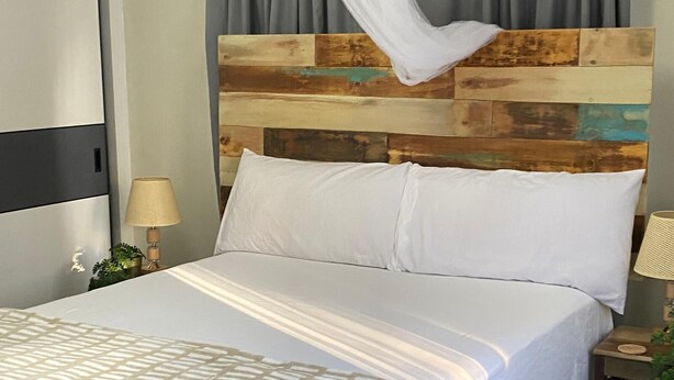 A bed with a white bedspread and pillows, a wooden headboard, a bedside lamp, and a small plant.